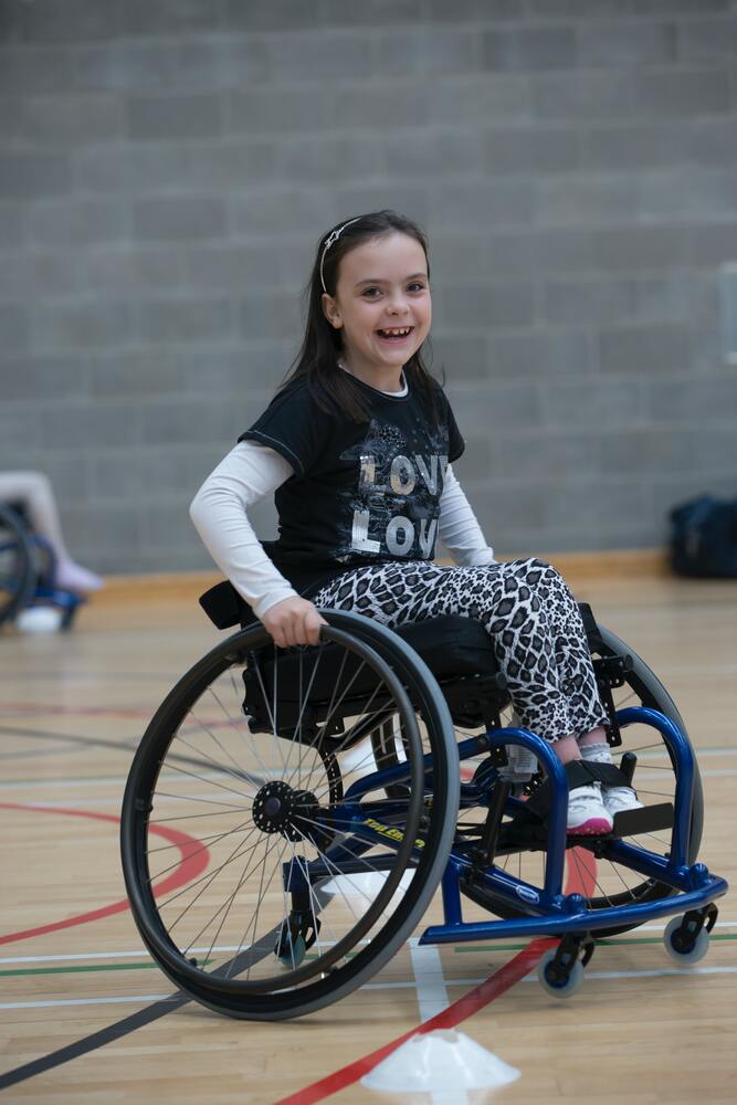 little girl in gym class smiling and using her wheelchair