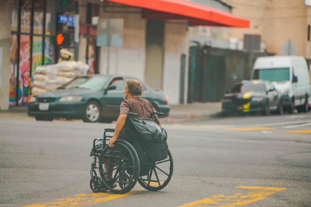 man using a wheelchair crosses the street in the crosswalk.