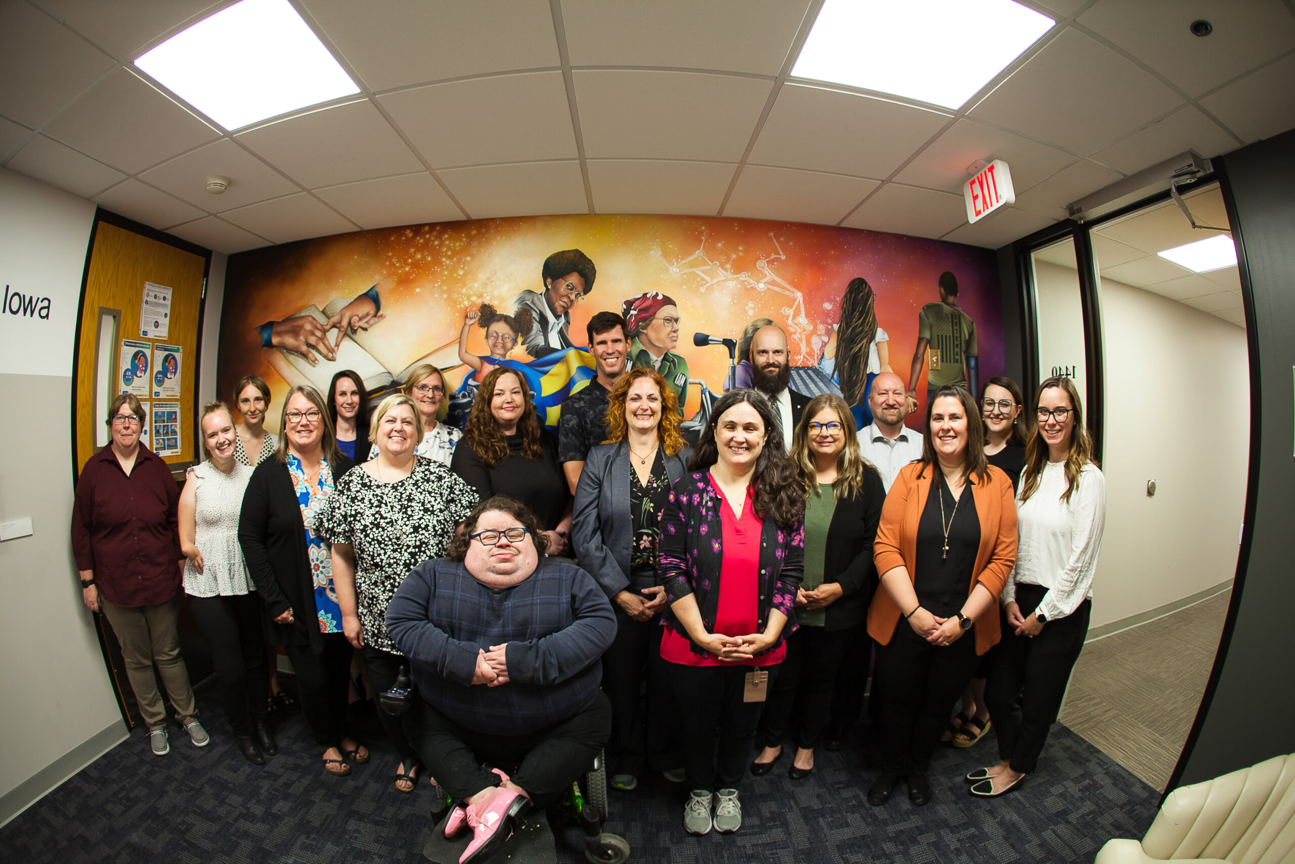 group photo of office staff standing and sitting in front of our Jill Wells disability inclusion mural.
