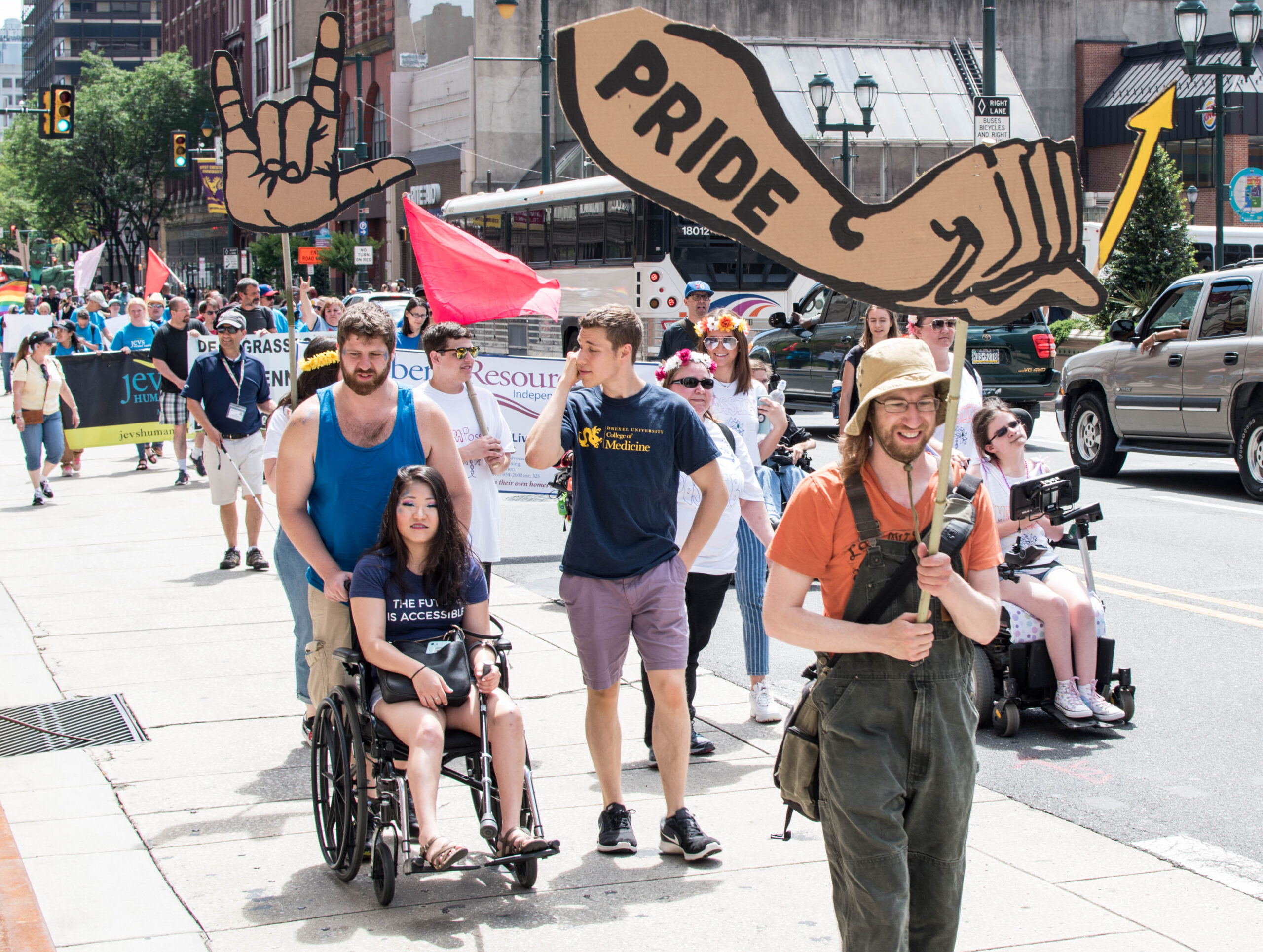 People with disabilities protesting with cardboard signs shaped like hands signing love and pride