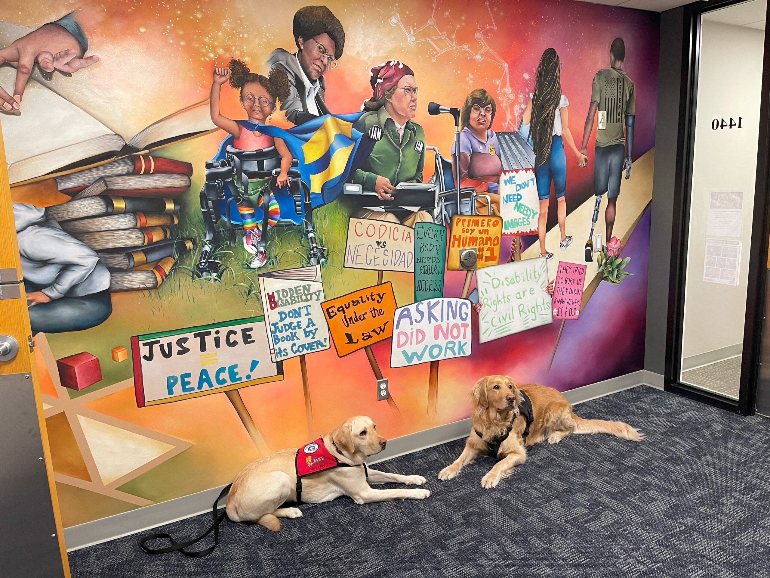 two dogs lay in front of a colorful disability rights mural