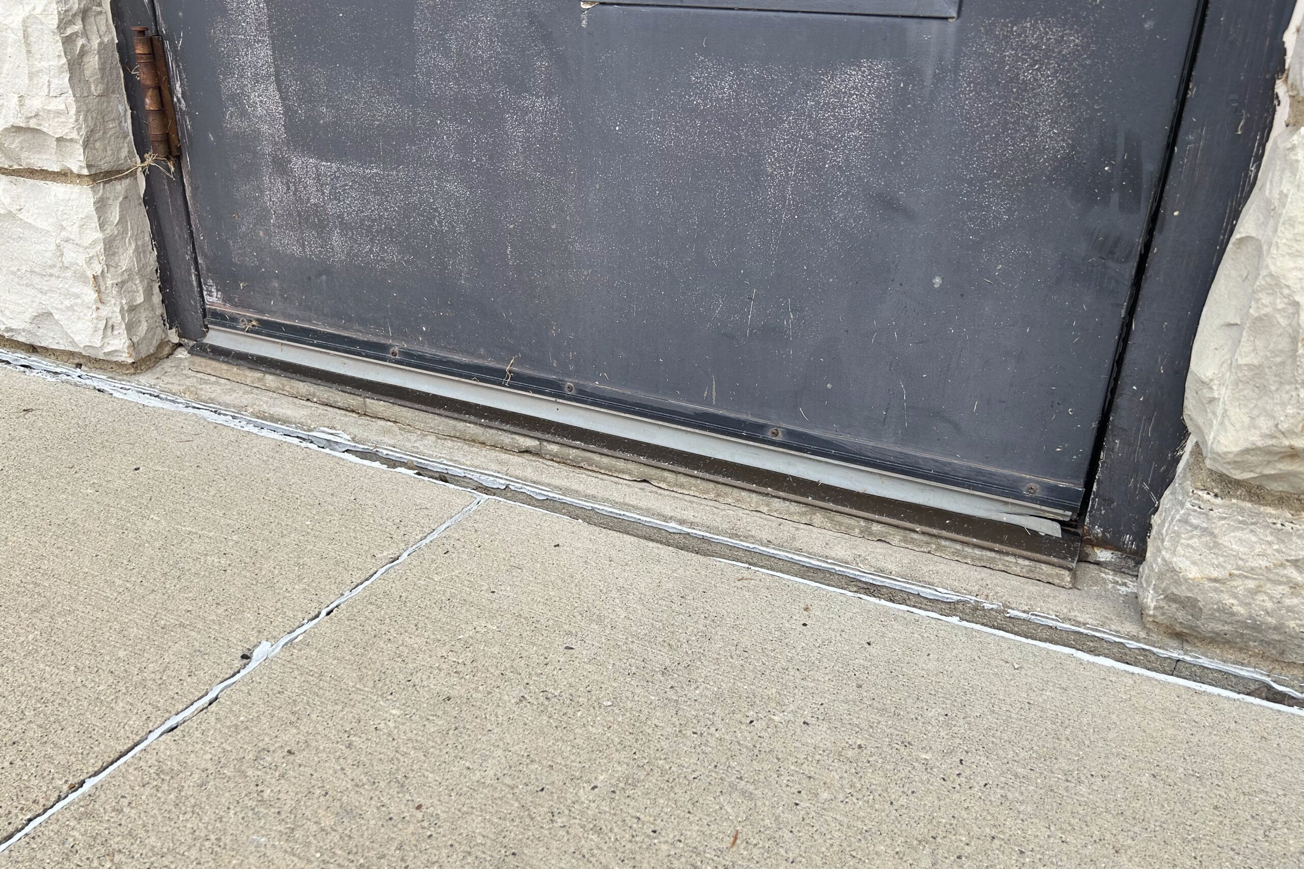 bottom of door, showing how the door is raised up on a one inch step, creating an accessibility barrier to entry.