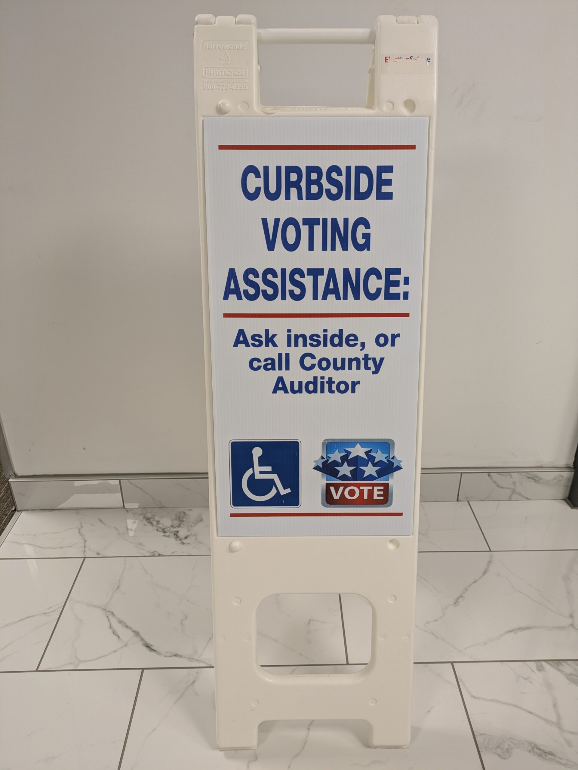 plastic sign with text about curbside voting assistance information printed on it
