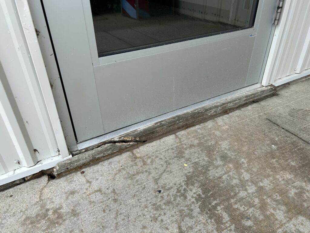 entryway with a broken ledge holding the door several inches above the ground, making it inaccessible.